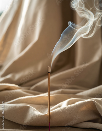 Burning incense stick on wooden holder with glowing ember and graceful smoke trail, minimalist lifestyle scene in bright sunny room for mindfulness, aromatherapy and zen home wellness