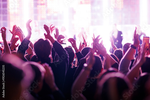 Crowds cheering with raised hands at bright music concert