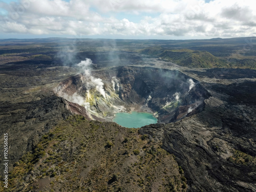 Aerial view of an active volcanic crater with a turquoise lake and steam rising from the vents.