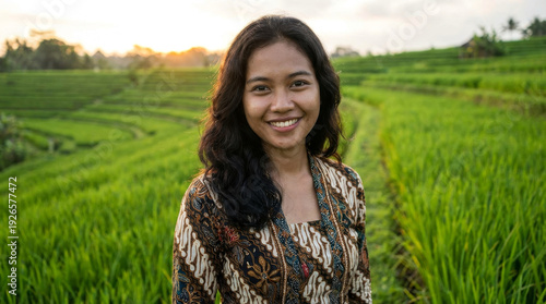 Young Indonesian woman smiling in a lush green rice paddy field at sunset.