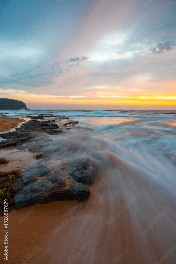 Naklejka premium Wave water flowing into the sandy and rocky beach shore.