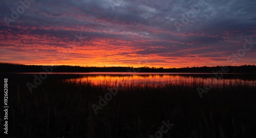 Striking sunset colors mirrored on a lake with shadowy foreground in gentle blur perfect nature backdrop