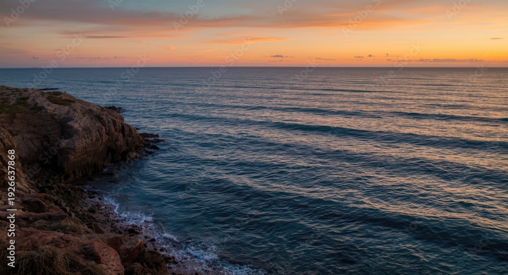Fototapeta premium Warm sunset hues highlighting craggy shoreline and rhythmic waves in a picturesque seashore