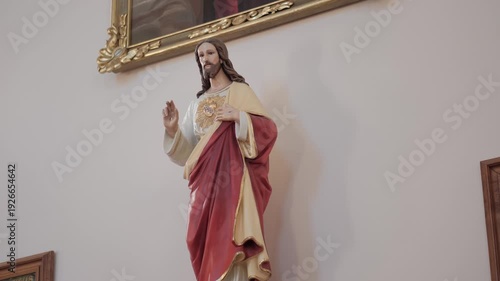 Statue of the Sacred Heart of Jesus mounted on a white wall in a church interior. Static low angle shot.