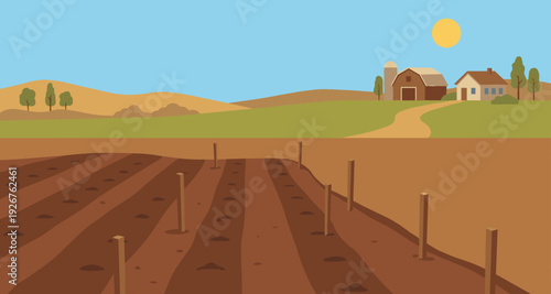 Plowed agricultural field with tilled rows prepared for spring planting in a rural landscape with a farm, barn, and silo on rolling hills under a sunny sky