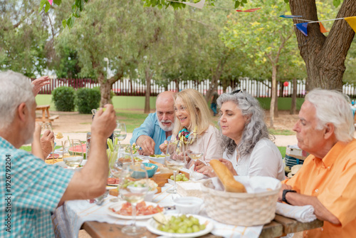 Group of diverse seniors sharing food and drinks at a festive garden table