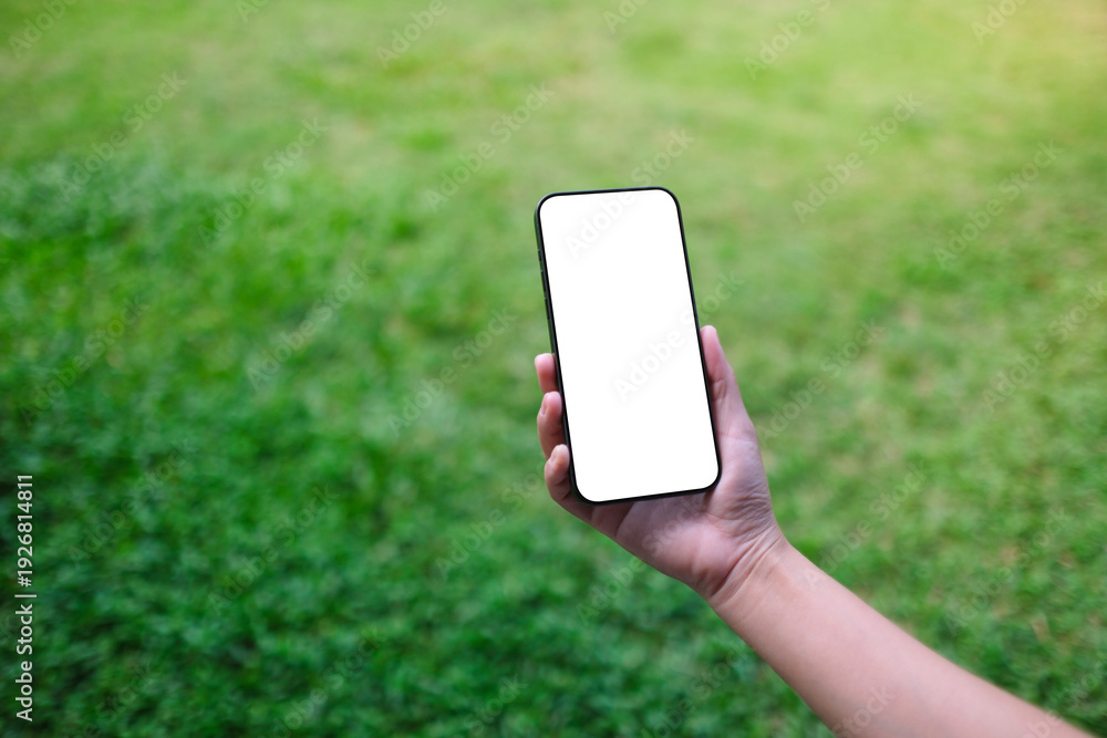 Fototapeta premium Mockup image of a woman holding mobile phone with blank desktop screen in the green yard