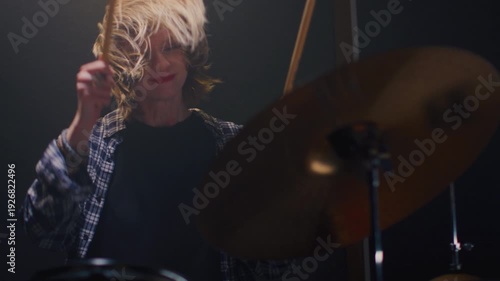 Young girl blonde rock is playing the drums on concert stage. Woman bangs on a drum kit. Face of female musician bangs drumsticks in a snare drum, cymbals in rehearsal studio, repetition. Portrait