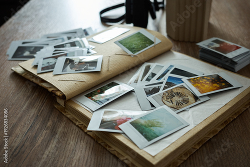 Collection of old photographs scattered on a wooden table with a camera nearby and a stack of more pictures beside them