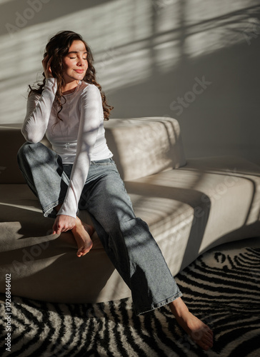 Bild auf Leinwand Woman seated on a sofa in a bright room with shadows on the wall
