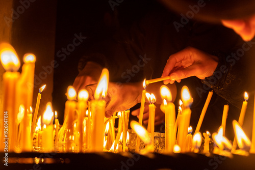 Canvas Print Many hands of people light and place candles in church, leaving numerous burning candles at Christian altar
