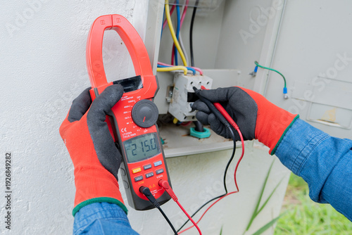 Photography Close-up of an electrician's hands using a clamp meter to measure the flow of el