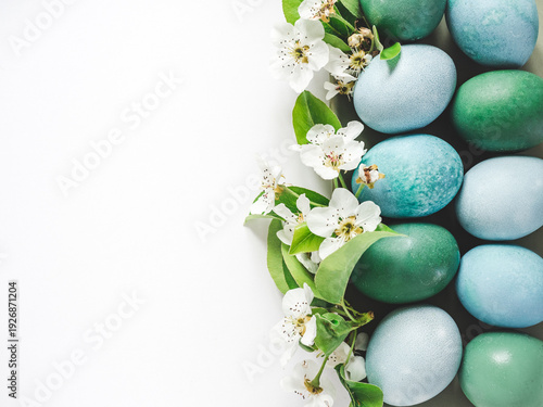 Pastel blue Easter eggs on a white table with spring blossoms. Festive Easter and spring celebration concept. Flat lay, minimalist style, copy space. Close-up, view from above