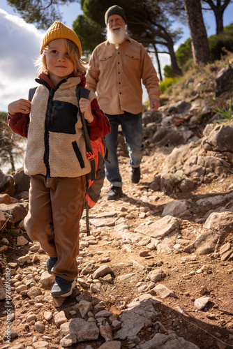 Canvas Print Confident young boy hiking downhill on rocky mountain trail with backpack, follo