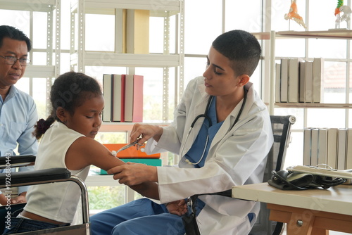 A pediatrician holds a syringe and administers a flu vaccine to a young African-American girl sitting with her father at the hospital.

