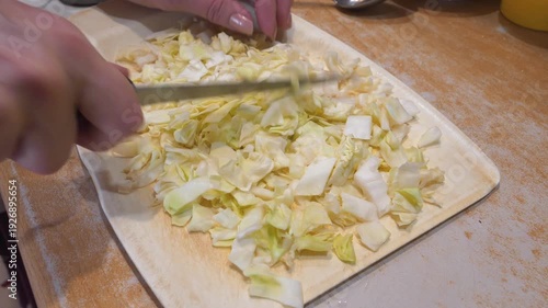 Female cook cutting white cabbage on a kitchen board for cooking vegetable stew. Woman cuts white cabbage with a knife on a cutting board to prepare Ukrainian borscht

