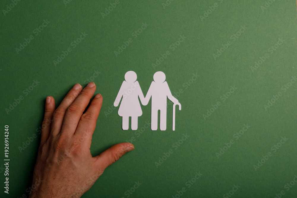Fototapeta premium An image of an elderly couple cutout on a green background with a hand reaching towards them, evoking themes of care and