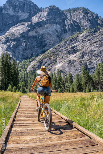A woman is riding a bicycle on a wooden bridge over a grassy field