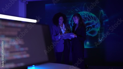 Diverse female data scientists collaborating on artificial intelligence algorithms. Computational neuroscientists discussing digital brain network via tablet.