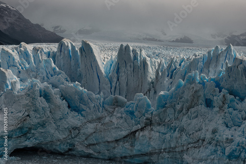 Obraz na plátně Detailed view of jagged blue ice pinnacles and deep crevasses on a massive glacier surface under a foggy mountain sky in Patagonia