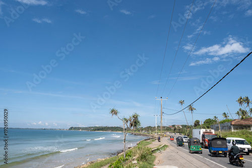 12.06.2025 Matara, Sri Lanka. Traditional colorful tuk-tuk taxi driving on the scenic coastal road between Matara and Dondra, Sri Lanka. Tropical palm trees and Indian Ocean in the background.