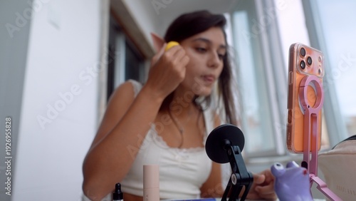 Woman in mirror applying blush with pleasant expression and daylight
