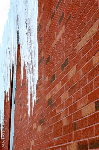 A row of long icicles hanging parallel to a red brick exterior wall.