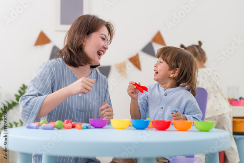 Photos Happy mother laughing with cute little boy while playing with colorful toys at home playroom