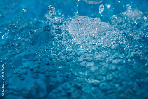 Macro shot of fresh blue water splashing with bubbles and water droplets. Abstract turquoise liquid background representing purity, freshness, and hydration. High-speed photography of water surface ri