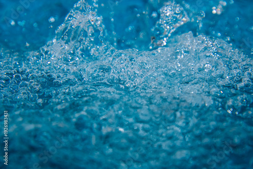 Macro shot of fresh blue water splashing with bubbles and water droplets. Abstract turquoise liquid background representing purity, freshness, and hydration. High-speed photography of water surface ri