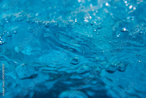 Macro shot of fresh blue water splashing with bubbles and water droplets. Abstract turquoise liquid background representing purity, freshness, and hydration. High-speed photography of water surface ri