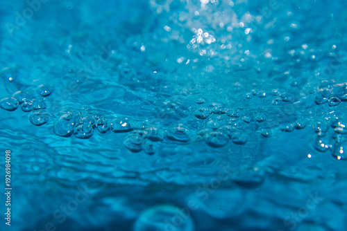Macro shot of fresh blue water splashing with bubbles and water droplets. Abstract turquoise liquid background representing purity, freshness, and hydration. High-speed photography of water surface ri