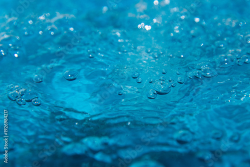 Macro shot of fresh blue water splashing with bubbles and water droplets. Abstract turquoise liquid background representing purity, freshness, and hydration. High-speed photography of water surface ri