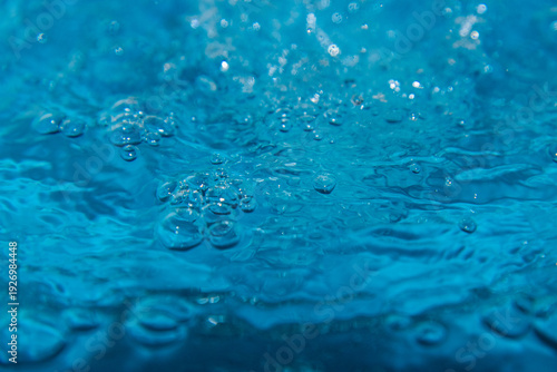 Macro shot of fresh blue water splashing with bubbles and water droplets. Abstract turquoise liquid background representing purity, freshness, and hydration. High-speed photography of water surface ri