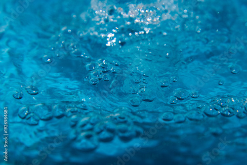 Macro shot of fresh blue water splashing with bubbles and water droplets. Abstract turquoise liquid background representing purity, freshness, and hydration. High-speed photography of water surface ri