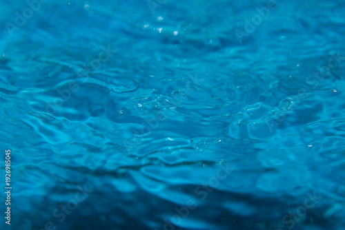 Macro shot of fresh blue water splashing with bubbles and water droplets. Abstract turquoise liquid background representing purity, freshness, and hydration. High-speed photography of water surface ri
