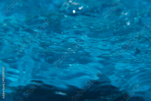 Macro shot of fresh blue water splashing with bubbles and water droplets. Abstract turquoise liquid background representing purity, freshness, and hydration. High-speed photography of water surface ri