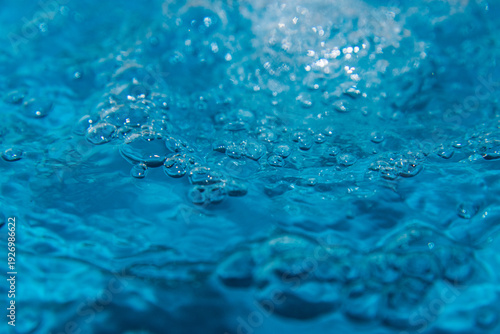 Macro shot of fresh blue water splashing with bubbles and water droplets. Abstract turquoise liquid background representing purity, freshness, and hydration. High-speed photography of water surface ri