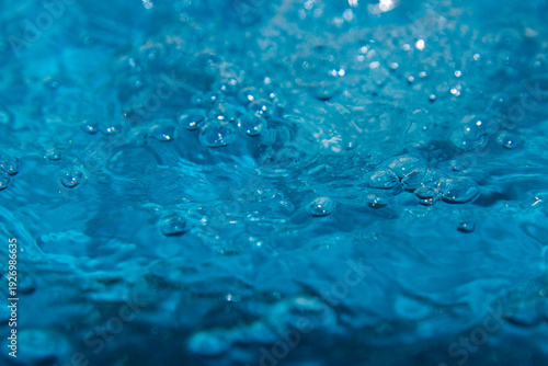 Macro shot of fresh blue water splashing with bubbles and water droplets. Abstract turquoise liquid background representing purity, freshness, and hydration. High-speed photography of water surface ri