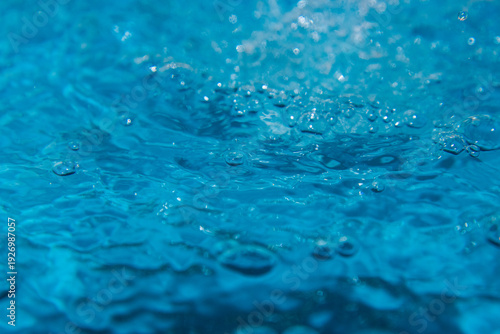 Macro shot of fresh blue water splashing with bubbles and water droplets. Abstract turquoise liquid background representing purity, freshness, and hydration. High-speed photography of water surface ri