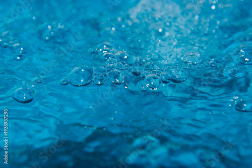 Macro shot of fresh blue water splashing with bubbles and water droplets. Abstract turquoise liquid background representing purity, freshness, and hydration. High-speed photography of water surface ri