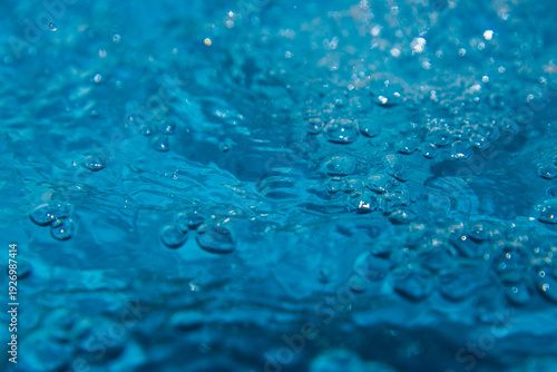 Macro shot of fresh blue water splashing with bubbles and water droplets. Abstract turquoise liquid background representing purity, freshness, and hydration. High-speed photography of water surface ri