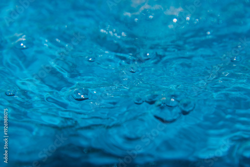Macro shot of fresh blue water splashing with bubbles and water droplets. Abstract turquoise liquid background representing purity, freshness, and hydration. High-speed photography of water surface ri
