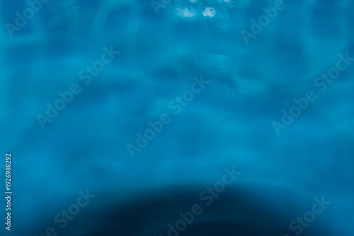 Macro shot of fresh blue water splashing with bubbles and water droplets. Abstract turquoise liquid background representing purity, freshness, and hydration. High-speed photography of water surface ri