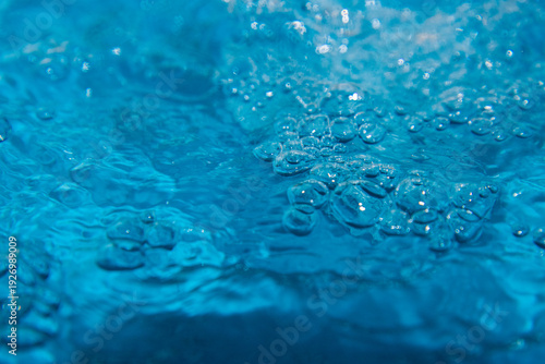 Macro shot of fresh blue water splashing with bubbles and water droplets. Abstract turquoise liquid background representing purity, freshness, and hydration. High-speed photography of water surface ri