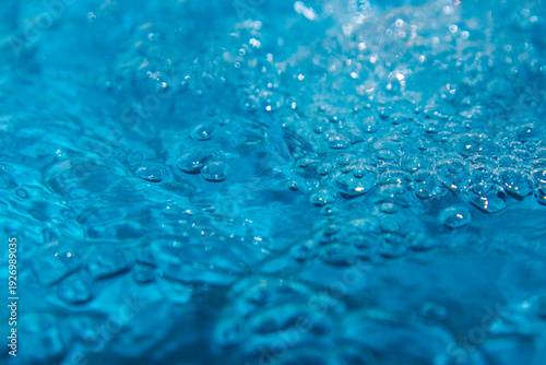 Macro shot of fresh blue water splashing with bubbles and water droplets. Abstract turquoise liquid background representing purity, freshness, and hydration. High-speed photography of water surface ri