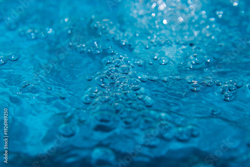Macro shot of fresh blue water splashing with bubbles and water droplets. Abstract turquoise liquid background representing purity, freshness, and hydration. High-speed photography of water surface ri