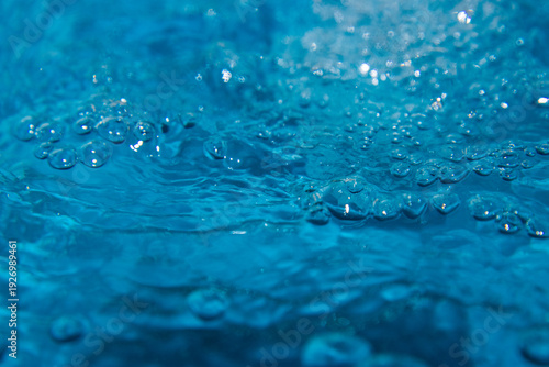 Macro shot of fresh blue water splashing with bubbles and water droplets. Abstract turquoise liquid background representing purity, freshness, and hydration. High-speed photography of water surface ri