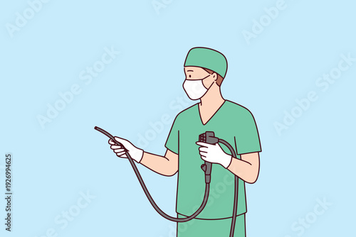 Male doctor in green medical scrubs and mask holds endoscope for colonoscopy or gastroscopy. Professional healthcare specialist preparing for cancer and polyp detection procedure.