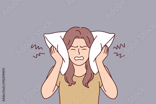 Irritated woman covers ears with pillow because of loud noise preventing her from sleeping. Suffering from insomnia, stress, and sleep disturbance in bedroom during dark night.